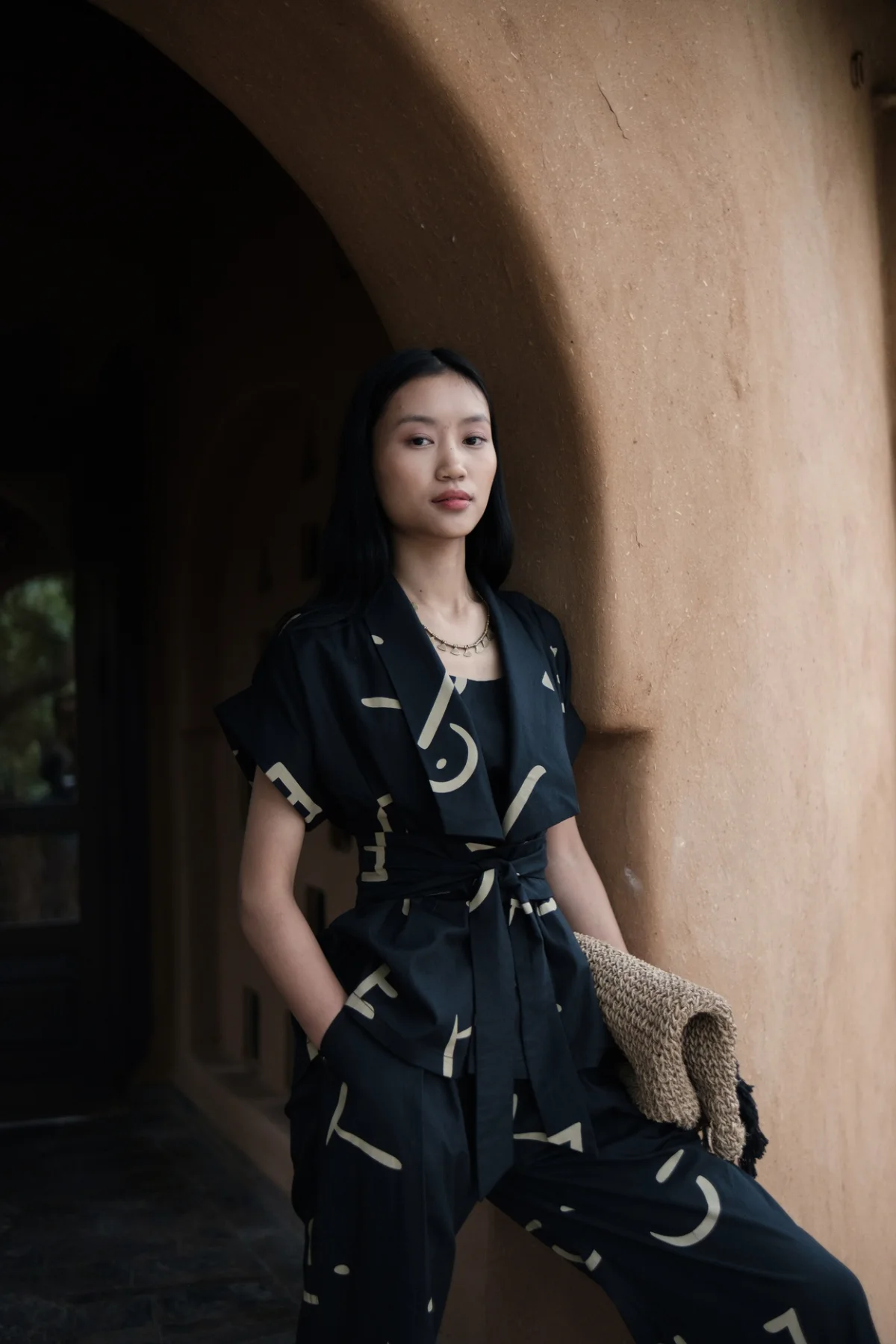 Model wearing a dark printed belted dress beneath an archway