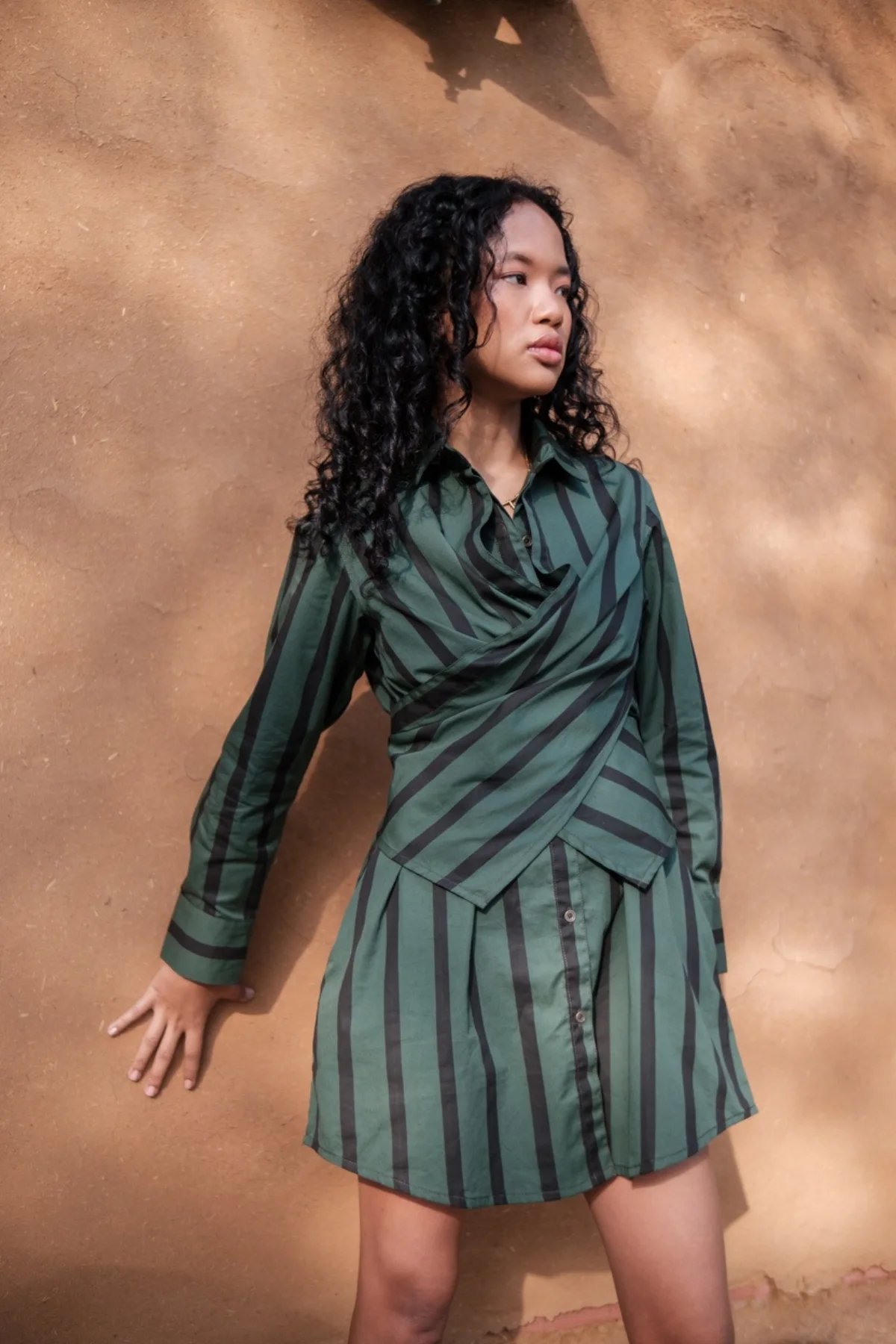 Model wearing a green striped wrap dress against an earthen wall