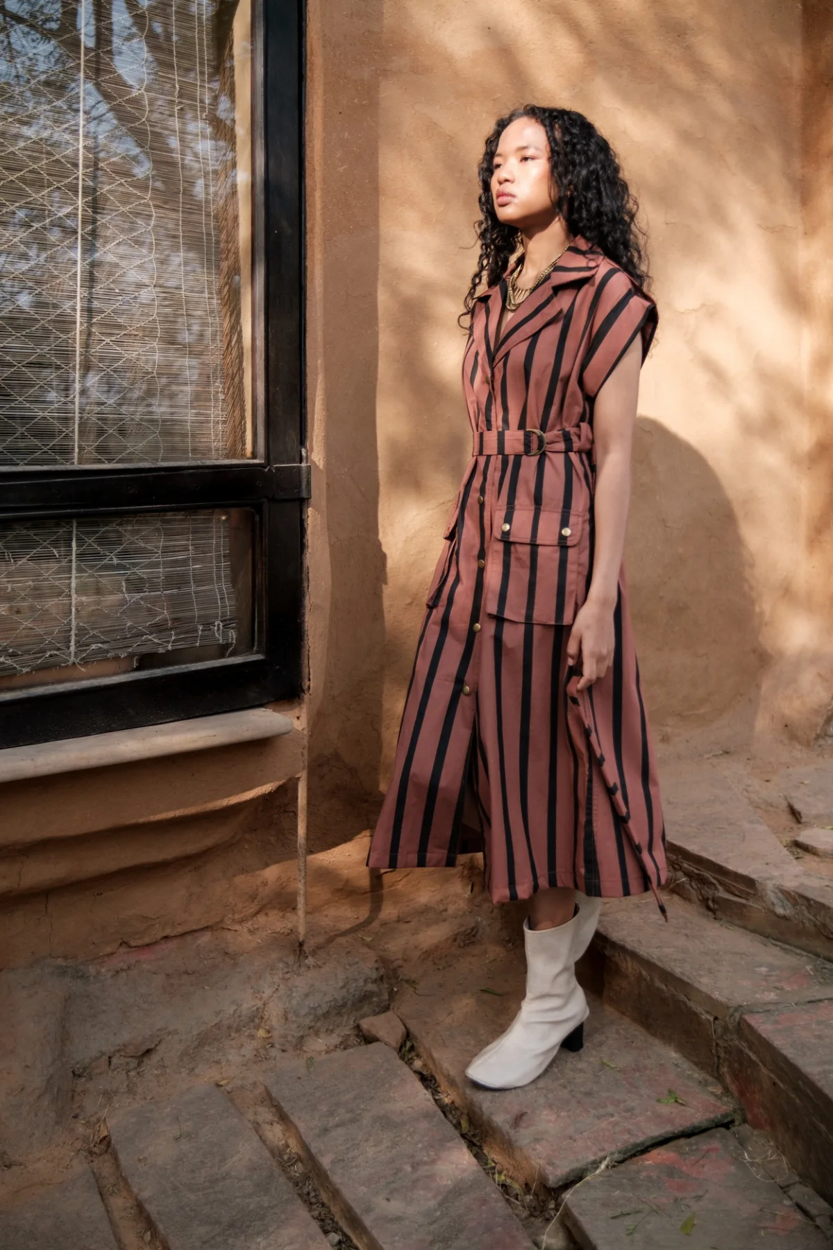 Model wearing a rust striped dress beside a window