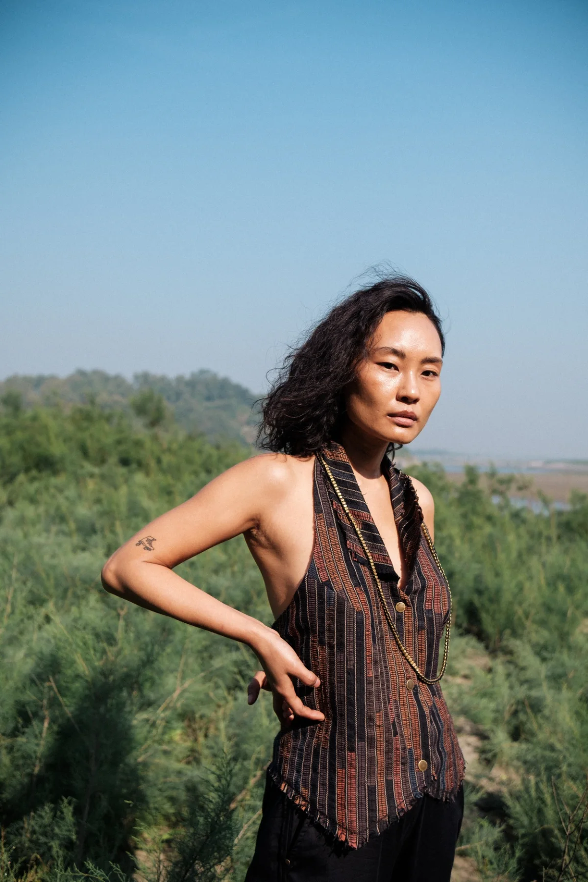 Model wearing a sleeveless dark textured top in a waterside landscape