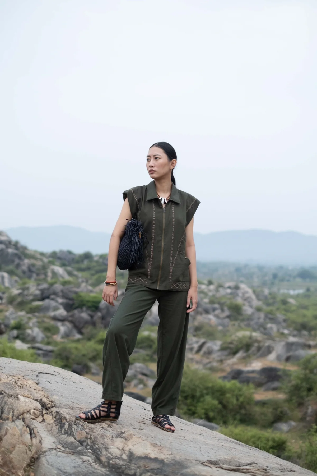Model wearing an olive sleeveless co-ord in a rocky landscape
